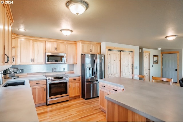 kitchen with light brown cabinetry, light wood-type flooring, light countertops, stainless steel appliances, and a sink