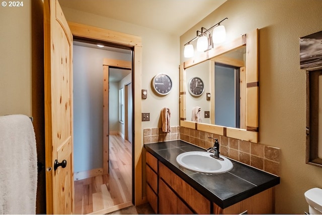 bathroom with decorative backsplash, wood finished floors, toilet, and vanity