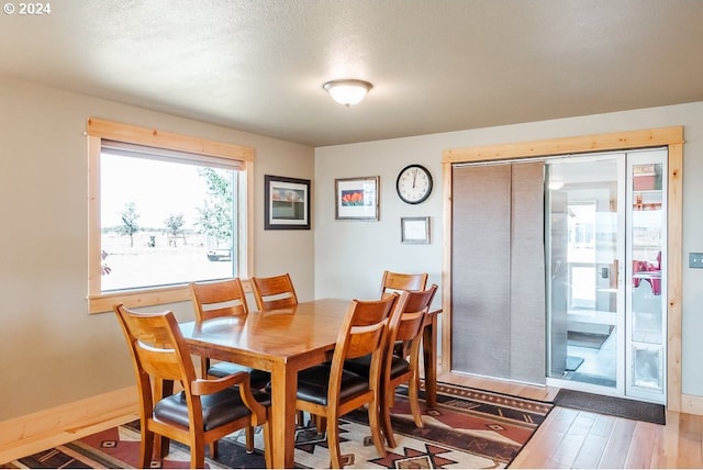 dining area with a textured ceiling, baseboards, and wood finished floors