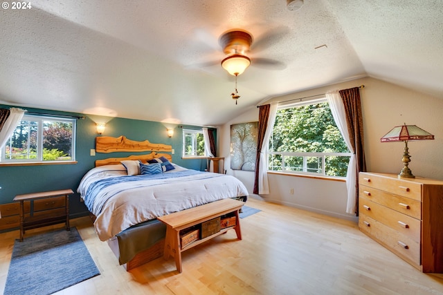 bedroom with ceiling fan, light hardwood / wood-style flooring, vaulted ceiling, and a textured ceiling