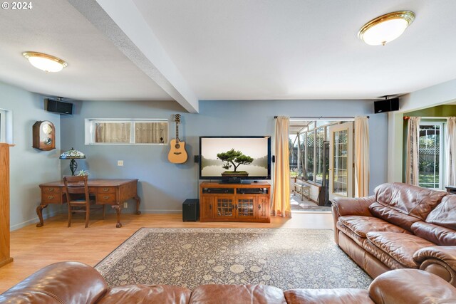 living room with a healthy amount of sunlight, beamed ceiling, and light wood-type flooring