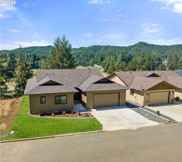 view of front of house with a garage, a front lawn, a wooded view, and concrete driveway