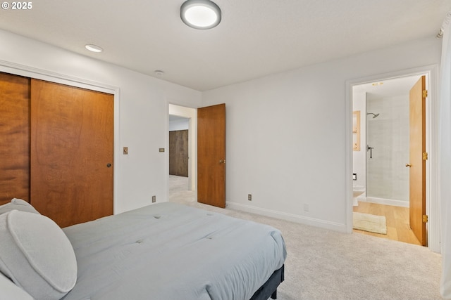 bedroom with a closet, light colored carpet, baseboards, and ensuite bathroom