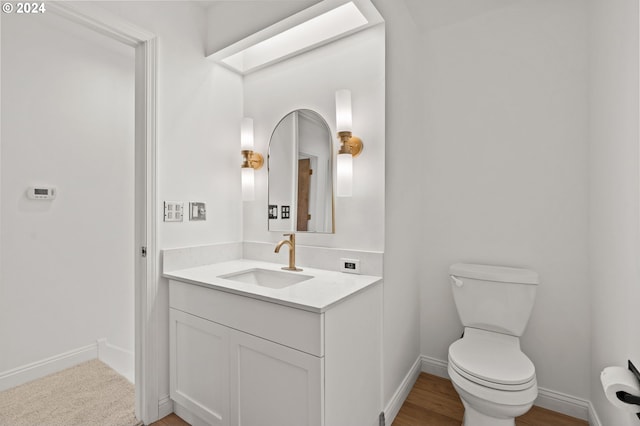 half bath with a skylight, baseboards, vanity, and toilet