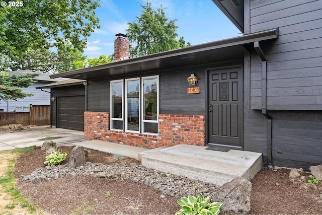 doorway to property with concrete driveway, brick siding, a chimney, and an attached garage