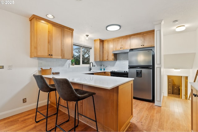 kitchen with black range with electric cooktop, under cabinet range hood, a peninsula, a sink, and stainless steel fridge