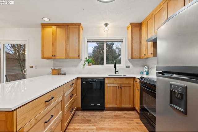 kitchen featuring light wood-style flooring, decorative backsplash, a sink, a peninsula, and black appliances