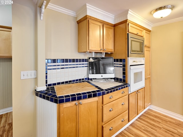 kitchen featuring stainless steel microwave, tasteful backsplash, light hardwood / wood-style flooring, tile countertops, and oven