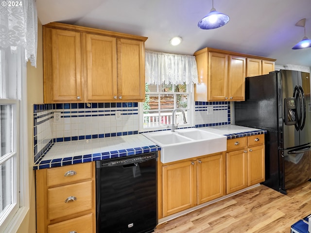 kitchen featuring black appliances, sink, light wood-type flooring, and tile counters