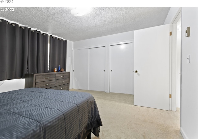 bedroom with a textured ceiling, light colored carpet, and multiple closets