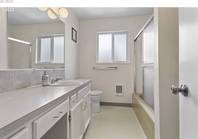 full bathroom featuring toilet, vanity, bath / shower combo with glass door, and heating unit