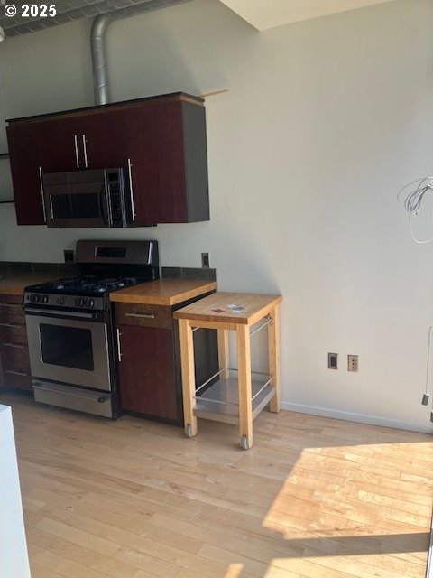 1410 SW 11th Ave Unit 402, Portland, OR 97201 - kitchen featuring stainless steel gas range, dark countertops, light wood-type flooring, and dark brown cabinets