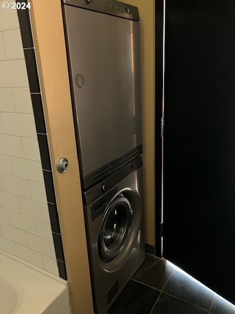 laundry room with stacked washer / dryer and dark tile patterned flooring