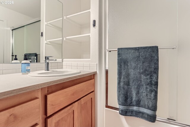 bathroom with combined bath / shower with glass door, vanity, and backsplash