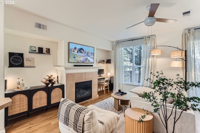 living room featuring ceiling fan, a tile fireplace, and light hardwood / wood-style floors