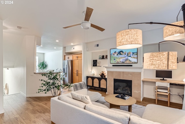 living room with a tiled fireplace, ceiling fan, and light hardwood / wood-style floors