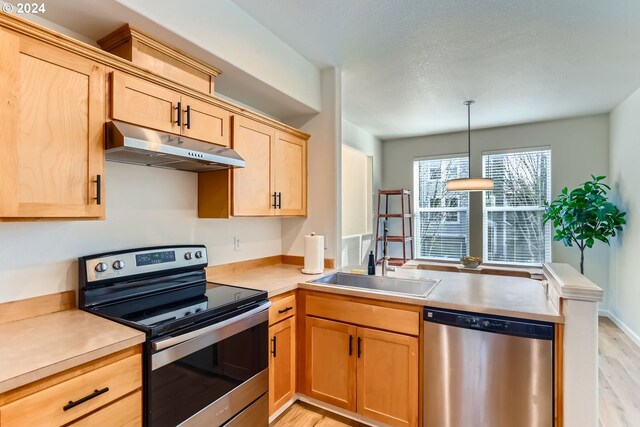 kitchen with light brown cabinetry, stainless steel appliances, sink, pendant lighting, and light hardwood / wood-style flooring