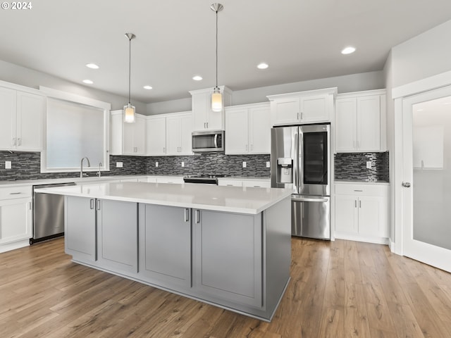 kitchen with decorative light fixtures, stainless steel appliances, white cabinets, and a kitchen island