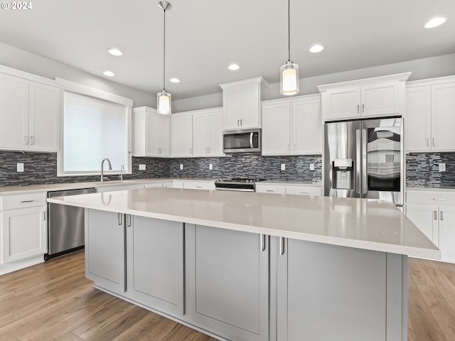 kitchen featuring a kitchen island, appliances with stainless steel finishes, decorative light fixtures, white cabinets, and light hardwood / wood-style flooring