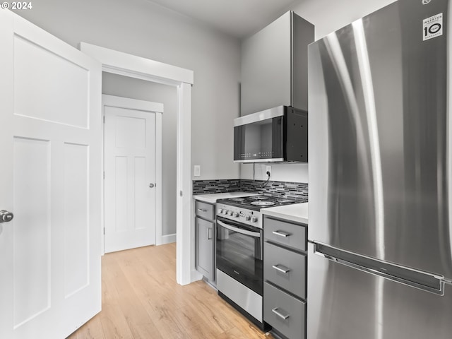 kitchen with tasteful backsplash, gray cabinets, stainless steel appliances, and light wood-type flooring