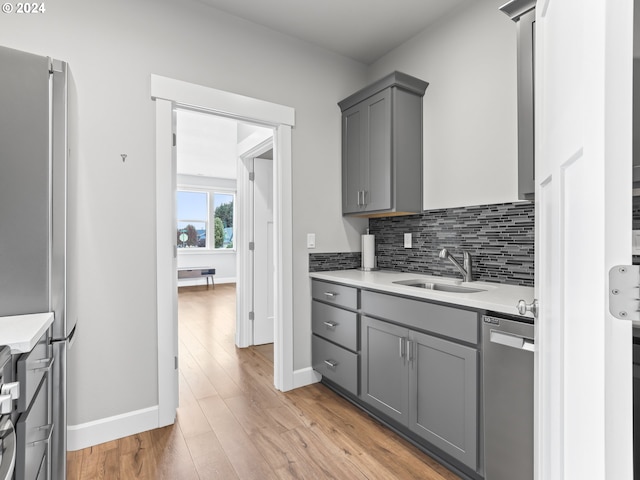 kitchen with appliances with stainless steel finishes, tasteful backsplash, sink, gray cabinetry, and light hardwood / wood-style floors