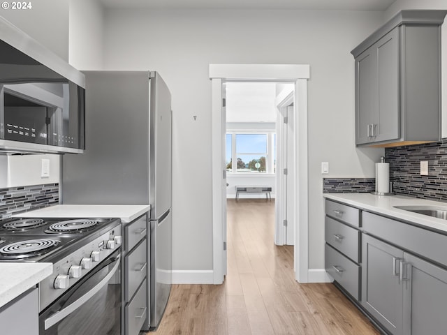 kitchen featuring tasteful backsplash, appliances with stainless steel finishes, gray cabinets, and light hardwood / wood-style flooring