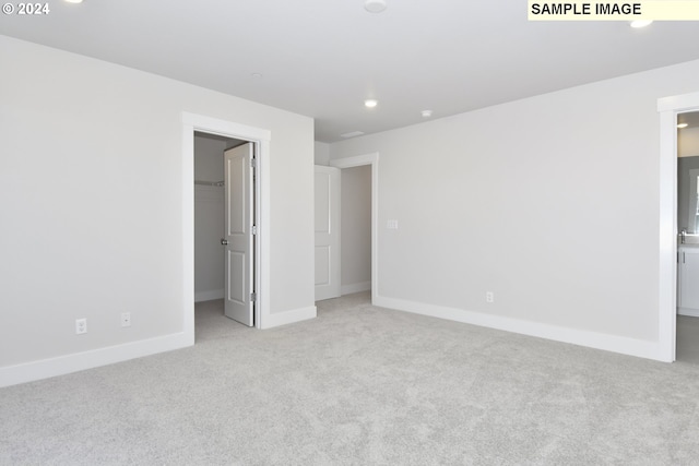 unfurnished bedroom featuring light colored carpet, ensuite bathroom, and a spacious closet