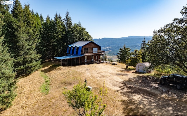 view of front of house with a deck with mountain view, a storage shed, a gambrel roof, and an outdoor structure