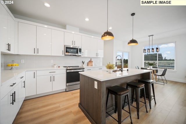 kitchen featuring sink, an island with sink, white cabinets, light hardwood / wood-style flooring, and appliances with stainless steel finishes