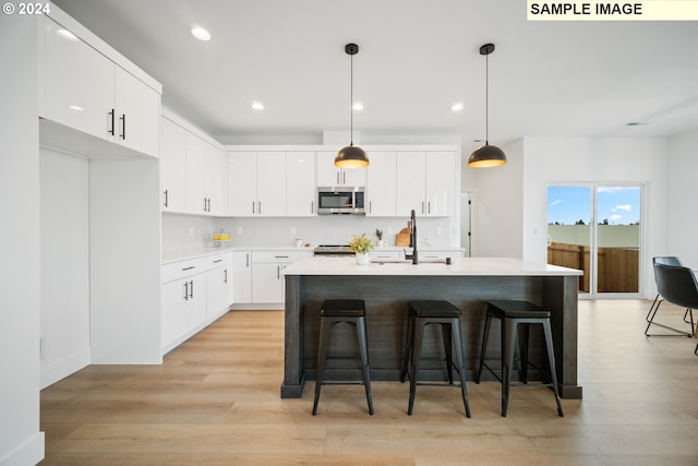 kitchen featuring appliances with stainless steel finishes, hanging light fixtures, light hardwood / wood-style floors, white cabinetry, and a center island with sink