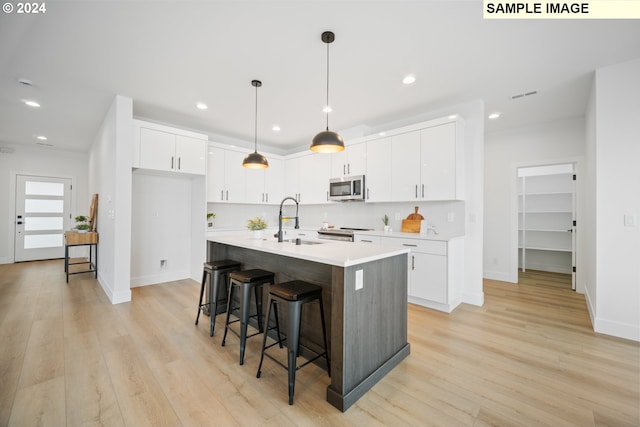 kitchen with an island with sink, sink, light hardwood / wood-style flooring, white cabinetry, and stainless steel appliances