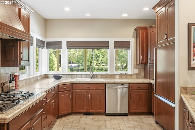 kitchen featuring appliances with stainless steel finishes, tile countertops, custom range hood, and backsplash