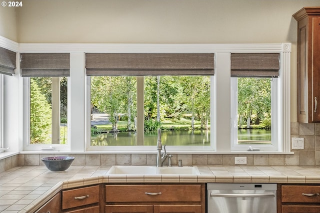 kitchen featuring dishwasher, a water view, sink, and tile countertops