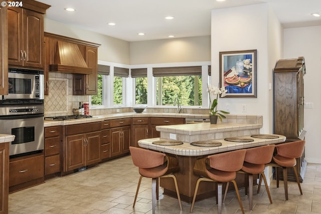 kitchen featuring tile counters, tasteful backsplash, a breakfast bar area, custom range hood, and appliances with stainless steel finishes