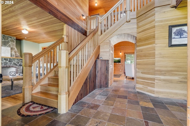 stairway featuring a stone fireplace, wooden walls, and wooden ceiling