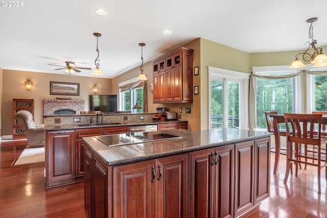 kitchen with pendant lighting, sink, dark stone countertops, a center island, and dark wood-type flooring