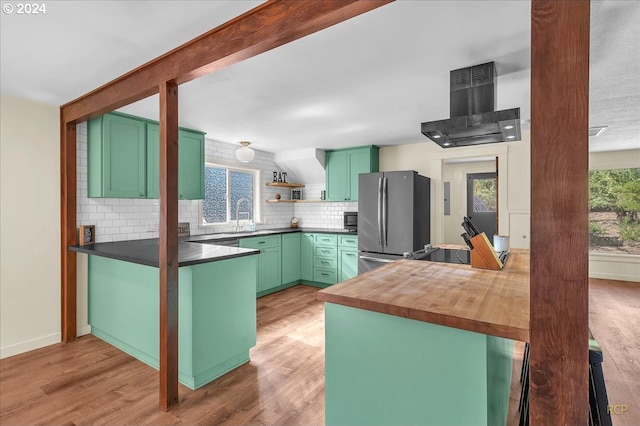 kitchen with green cabinets, hardwood / wood-style flooring, wood counters, stainless steel refrigerator, and range hood