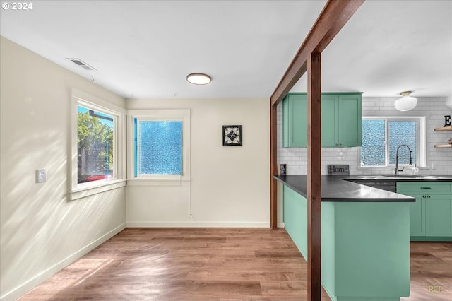 kitchen with sink, light hardwood / wood-style floors, green cabinets, and backsplash