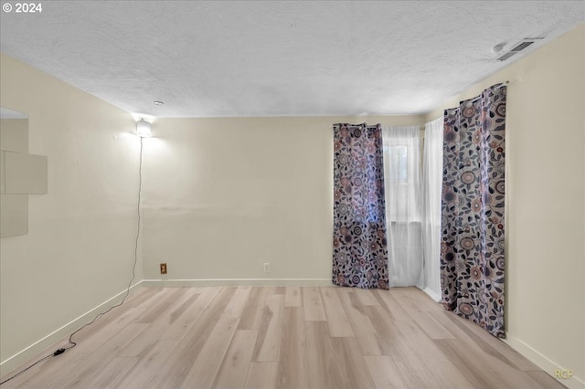 spare room with a textured ceiling and light wood-type flooring