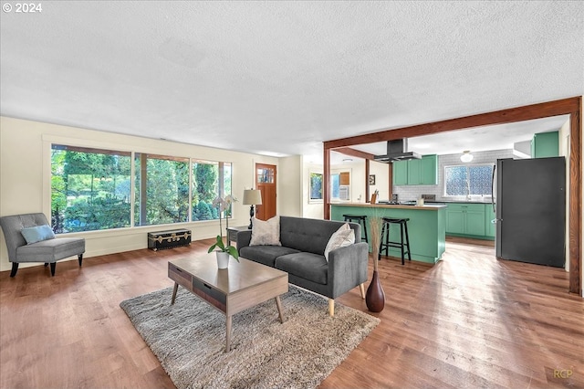 living room with wood-type flooring, a textured ceiling, ceiling fan, and beam ceiling