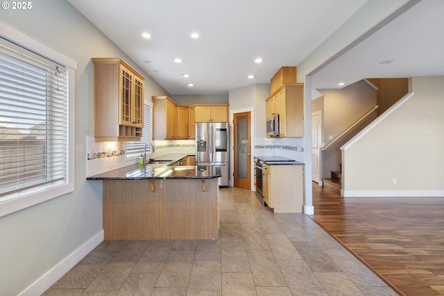 kitchen with baseboards, glass insert cabinets, a peninsula, stainless steel appliances, and a sink