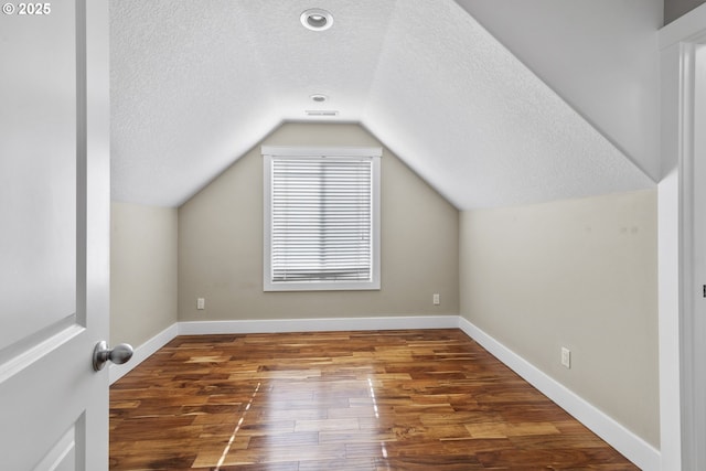 additional living space with a textured ceiling, lofted ceiling, wood finished floors, visible vents, and baseboards