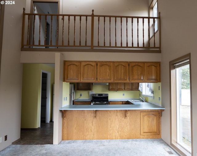 kitchen with light tile patterned floors, sink, stainless steel range with electric stovetop, kitchen peninsula, and a high ceiling