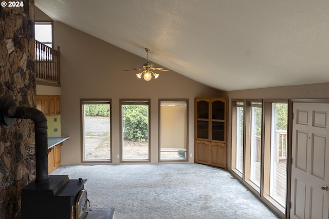 living room with a wealth of natural light, ceiling fan, a wood stove, and lofted ceiling