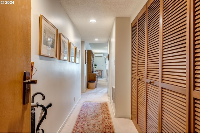 hallway with a wall unit AC, light carpet, and a textured ceiling