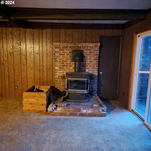 carpeted living room featuring wooden walls, beam ceiling, and a wood stove