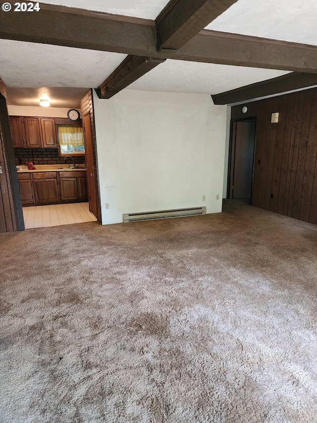 unfurnished living room featuring wood walls, baseboard heating, beam ceiling, sink, and light carpet