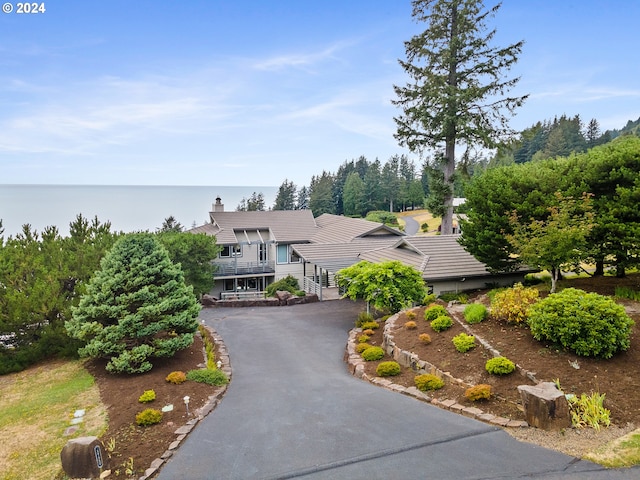 view of front of home with a tiled roof, a water view, driveway, and a chimney