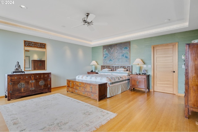 bedroom with light wood-style flooring, baseboards, and a raised ceiling