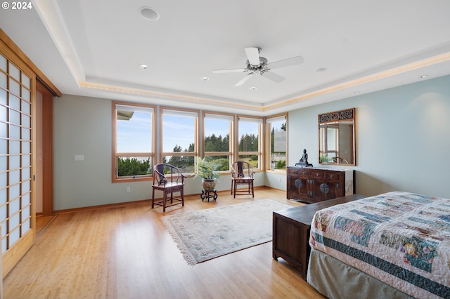 bedroom featuring light wood-type flooring, baseboards, and a raised ceiling